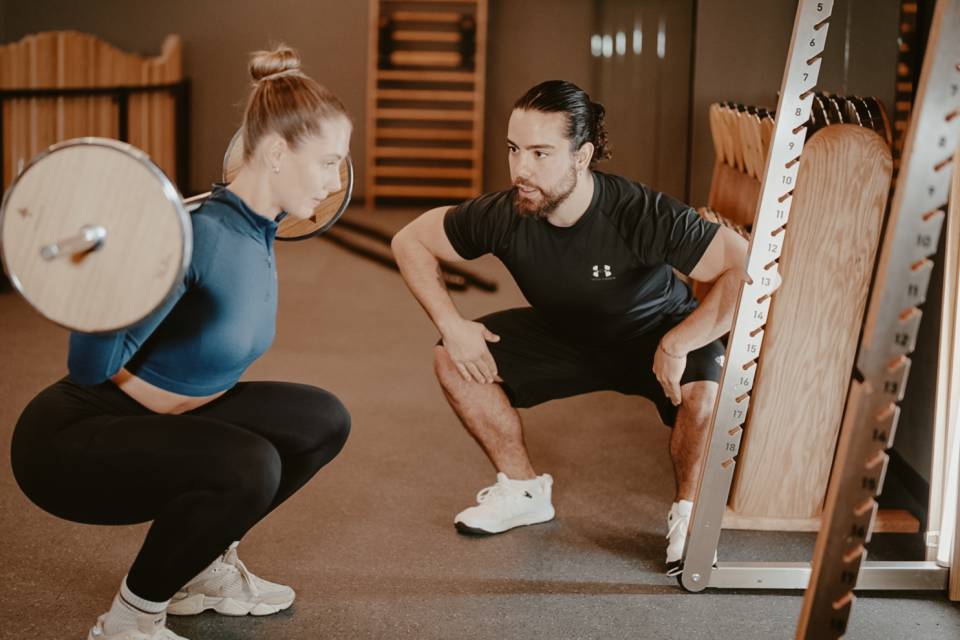 Trainer erklärt Frau Langhanteltraining im Aktivhotel Bergkristall