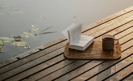 Buch mit einer Tassetee auf einem Steg am Teich